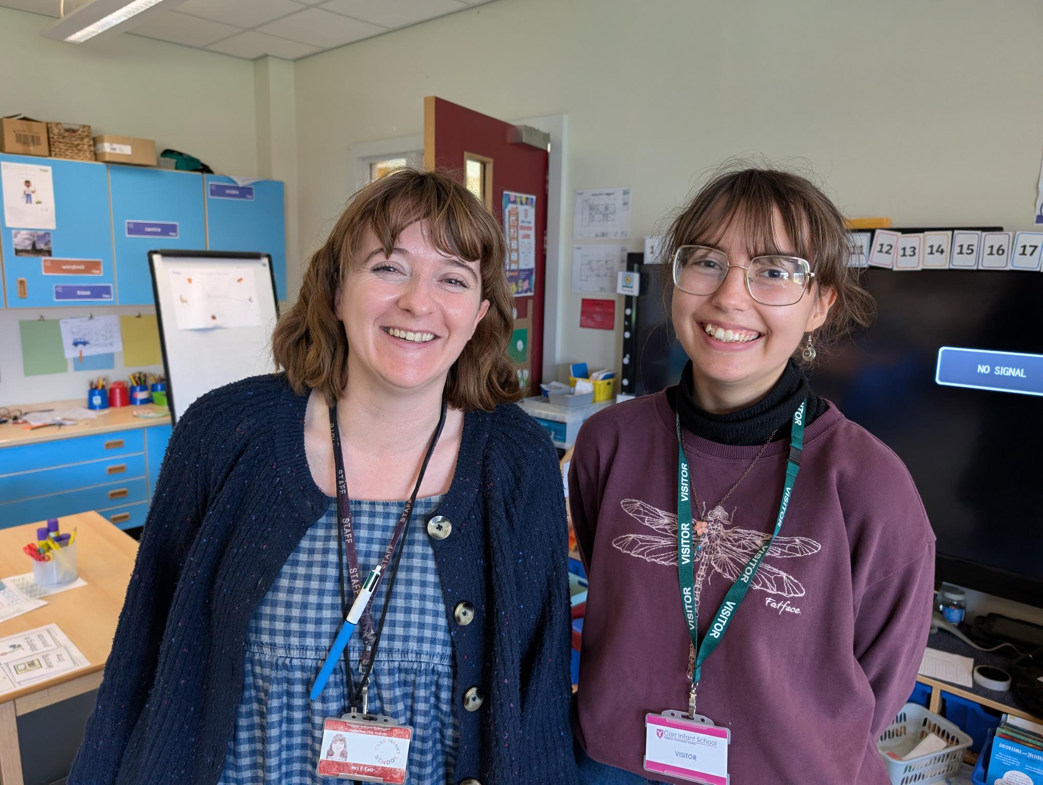 Climate Ambassador visiting infant school teacher. Both smiling as they meet in the classroom.