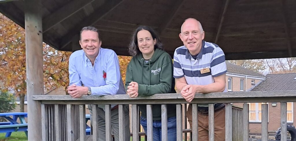 Chris, Clare and Richard leaning on the banister of a shaded are within the school grounds.