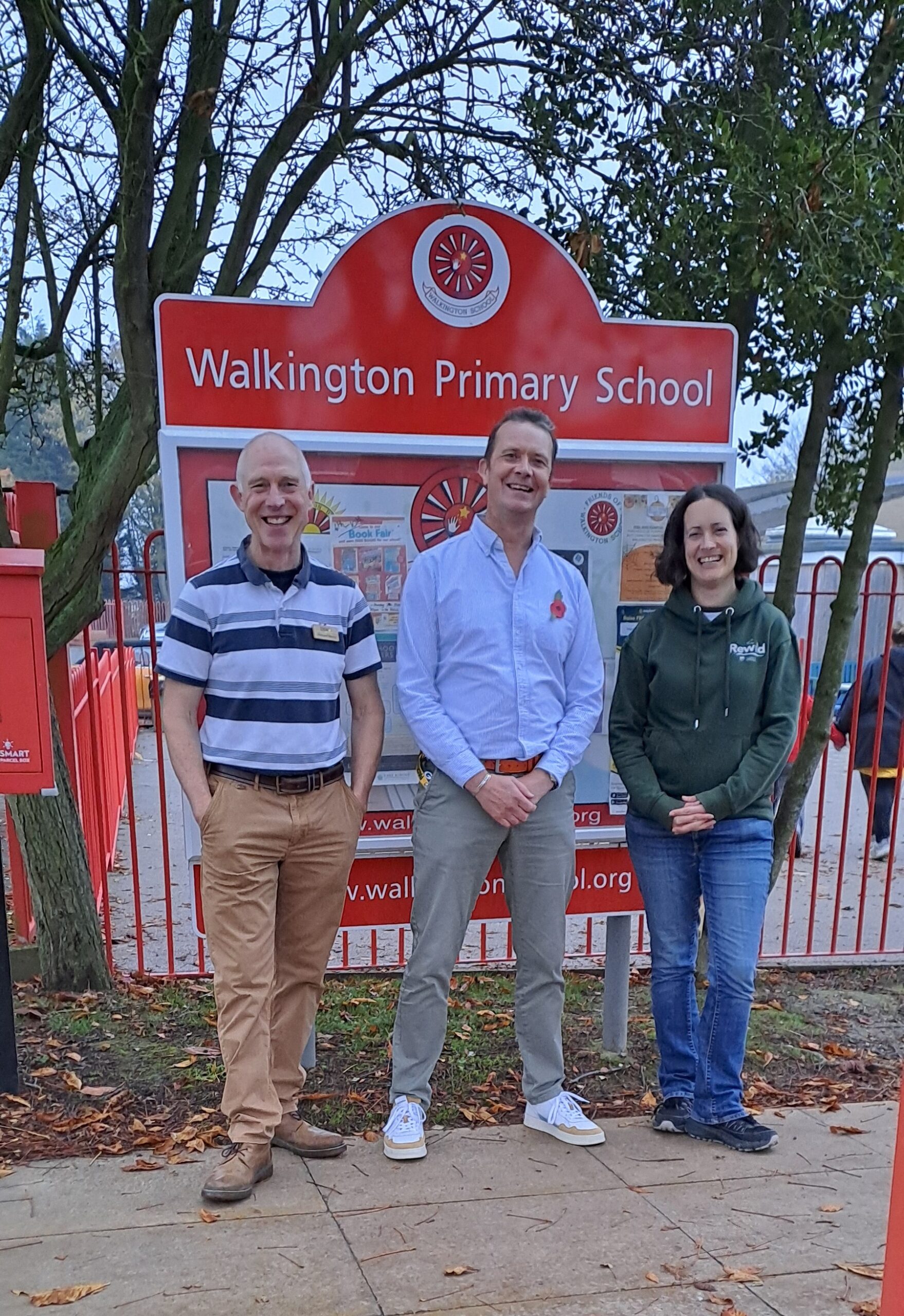Richard Berry, Chris Bullough and Clare Collins standing in front of the red Walkington Primary School sign smiling