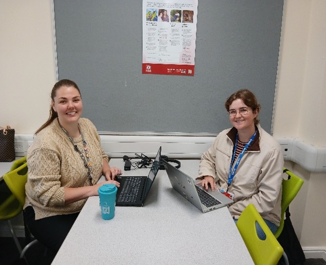 Natasha Wilkinson and Alana Thornton sat opposite each other at a desk working on the Climate Action Plan. Looking at the camera.