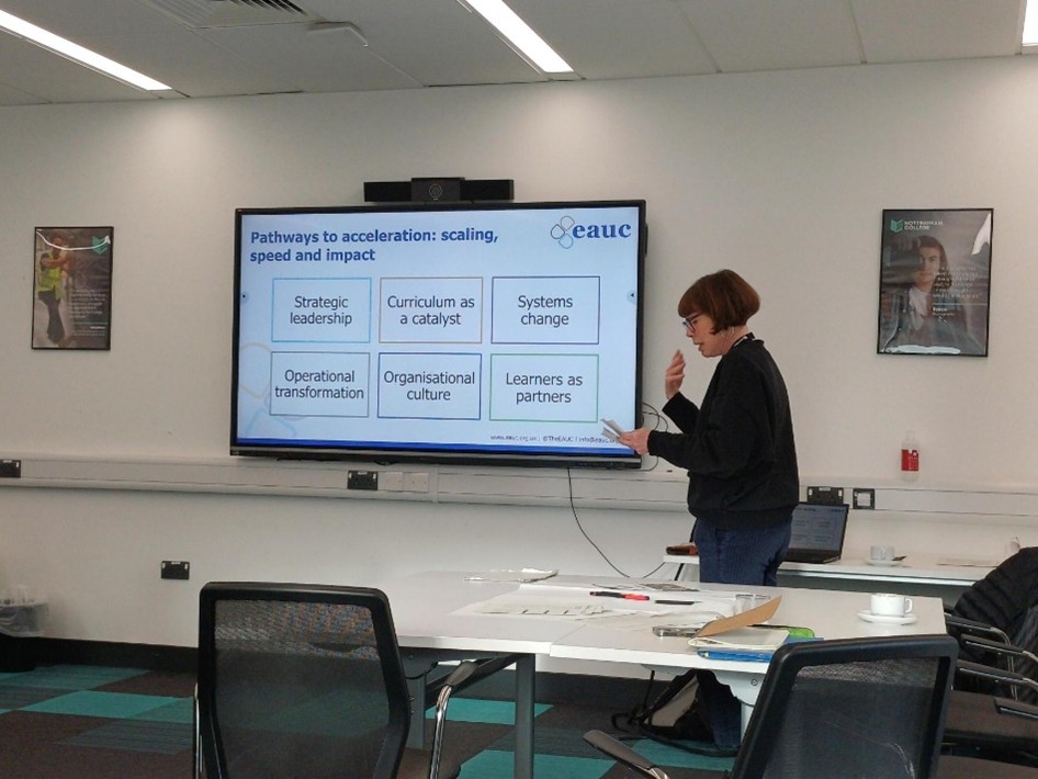 Jane Dickson standing beside a video screen giving a presentation to the attendees.